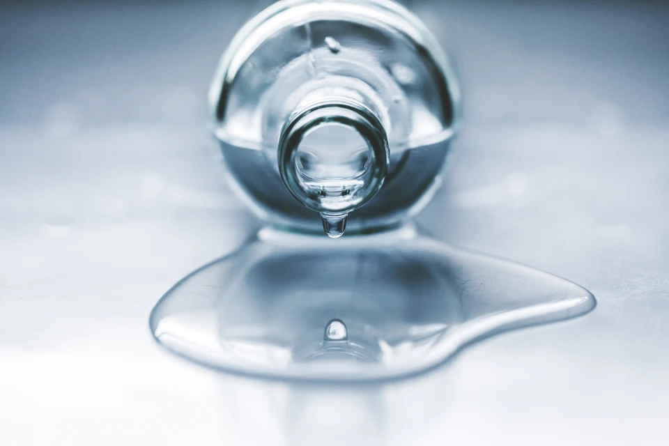 Beautiful image of one drop and its reflection. Bottle full of water, lying on the table. Water is spilled. Water drips.