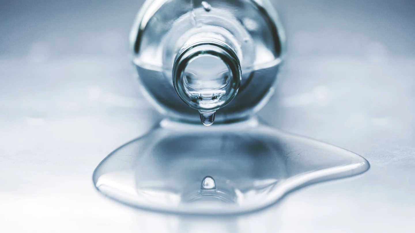 Beautiful image of one drop and its reflection. Bottle full of water, lying on the table. Water is spilled. Water drips.