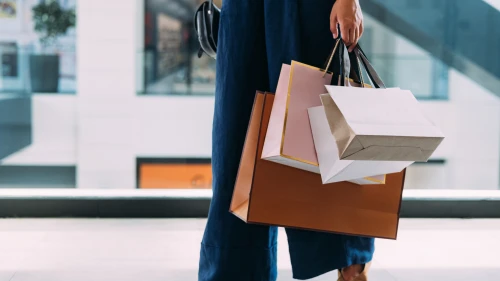 An unrecognizable Caucasian female standing at the shopping mall with paper bags.