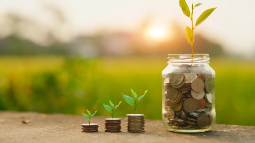 Saving money by hand puting coins in jug glass on nature background