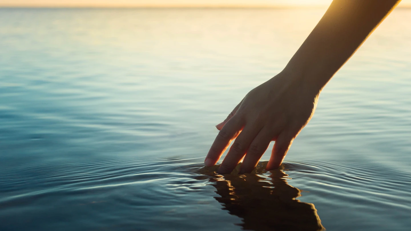 A female hand touching the ocean water in front of a beautful sunset during summer time.