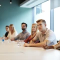 Group Of Young Candidates Sitting At Boardroom Table Listening To Presentation At Business Graduate Recruitment Assessment Day