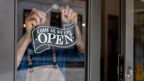 Close-up on a business owner hanging an open sign on the door of his restaurant - food and drink establishment concepts